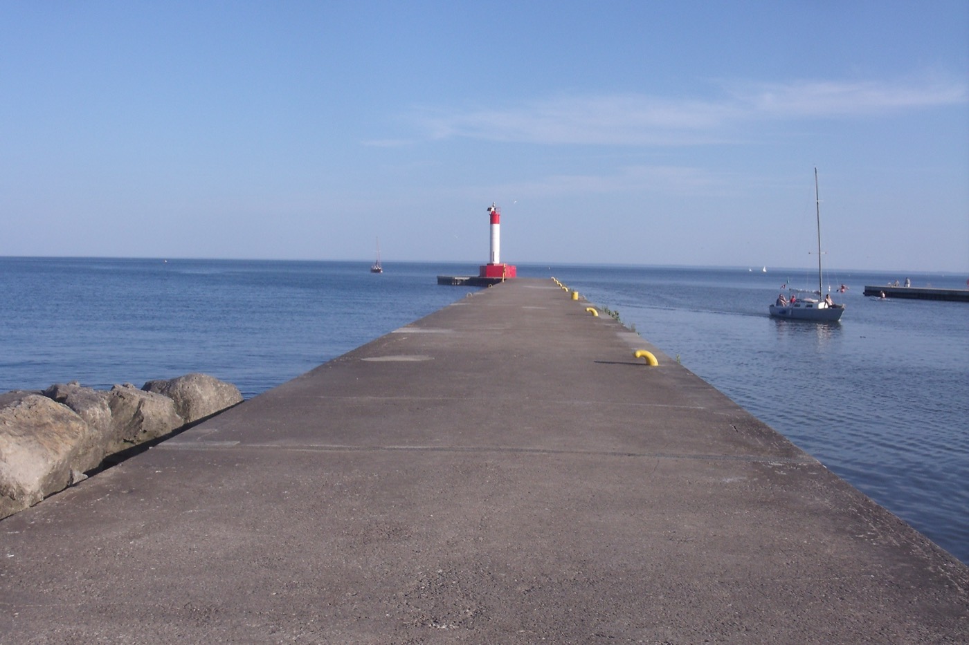 The pier and red-and-white lighthouse at Oakville Harbour on Lake Ontario, with a sailboat passing